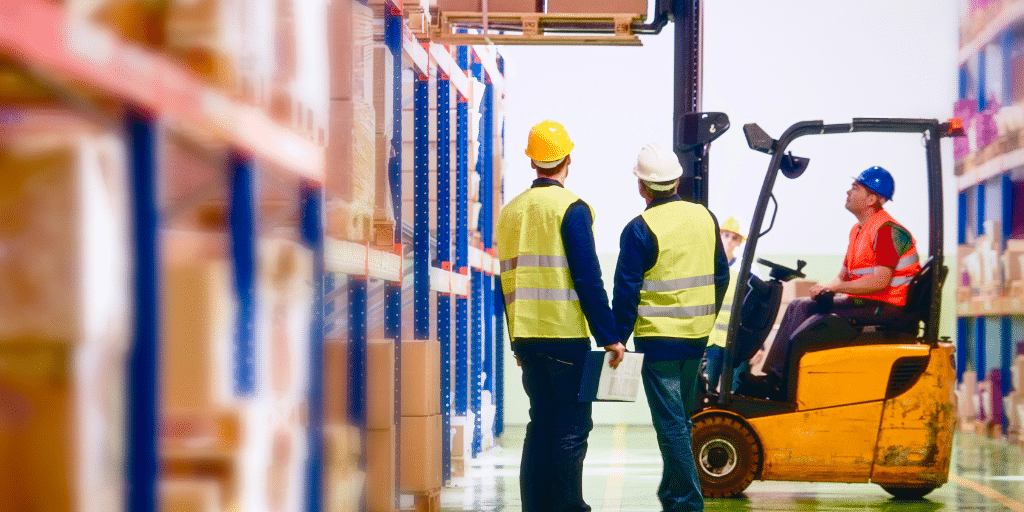 2 men in hi vis jackets in a warehouse. one man on a truck